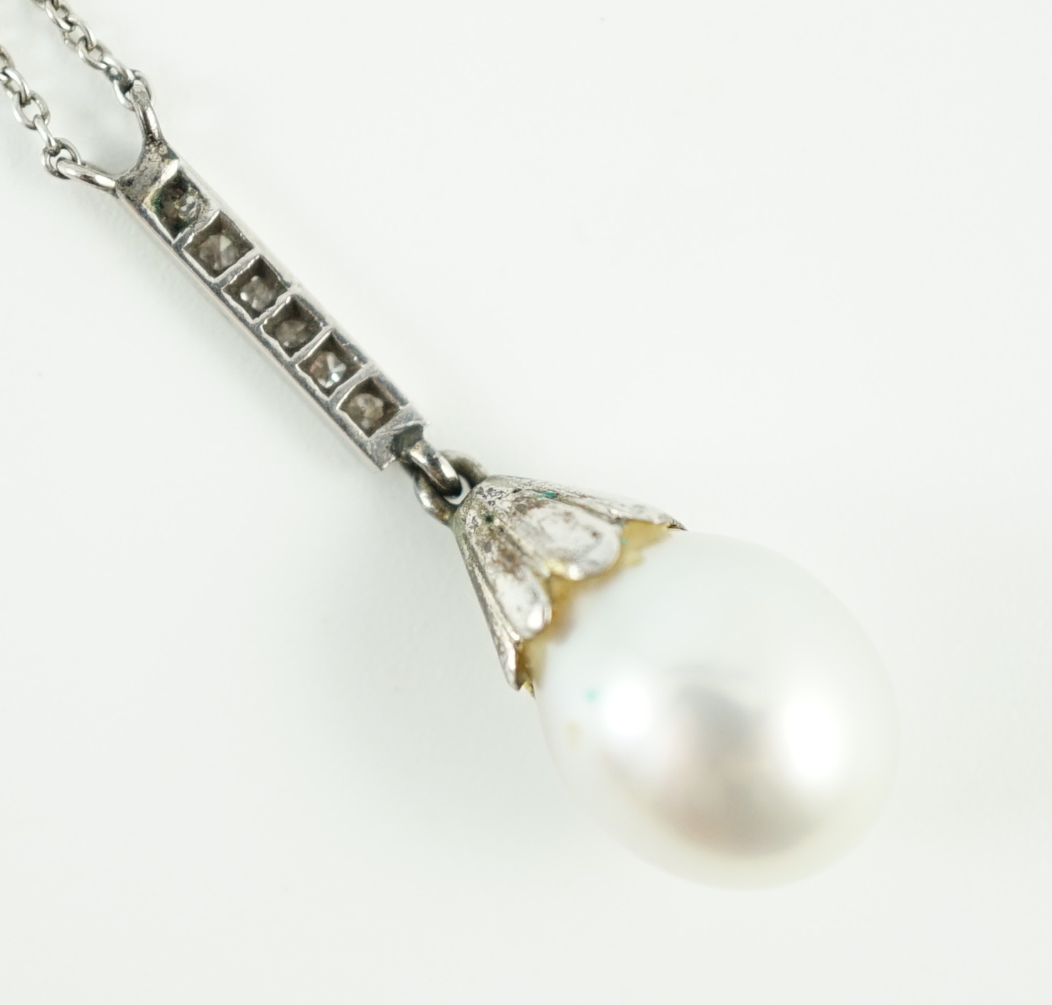 A 1920's platinum, single stone pear shaped cultured pearl and six stone diamond chip set pendant necklace